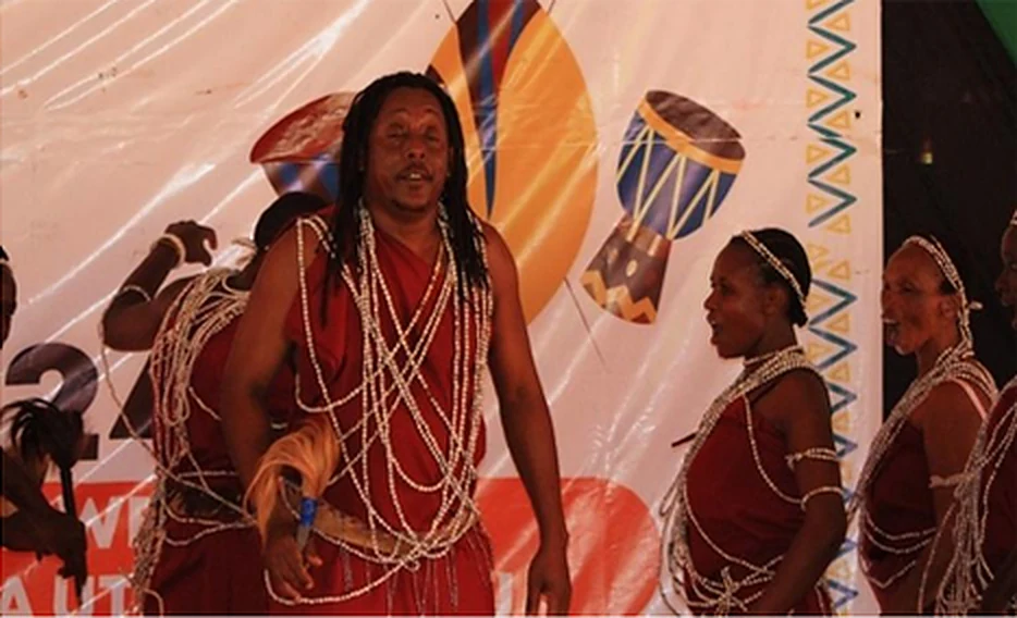 A Taveta performer in red attire and bead necklaces dancing the Uruasi.
